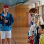 Diverse group of children standing indoors in a gym with a coach in focus.